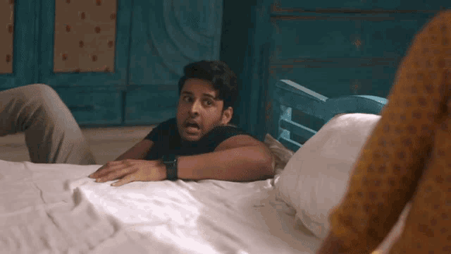 a man in a black shirt is laying on a bed with a surprised look on his face