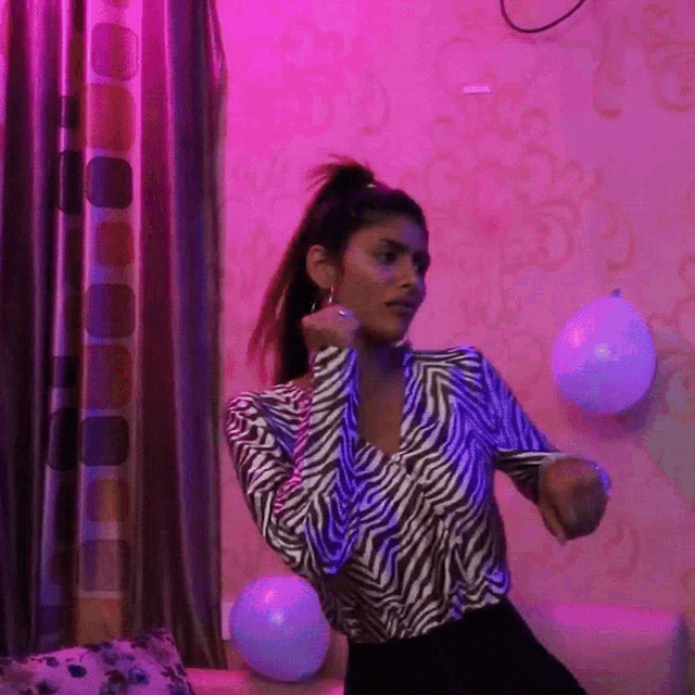 a woman in a zebra print top is dancing in a room with balloons