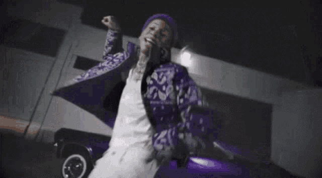 a man in a purple jacket and hat is standing in front of a purple car .