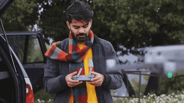 a man wearing a scarf and a jacket is holding a remote control