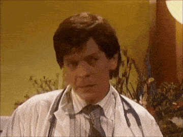 a man in a white coat and tie with a stethoscope around his neck is making a funny face .