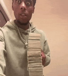 a man in a hoodie is holding a stack of money in his hands .