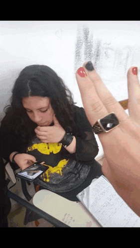 a girl wearing a batman shirt sits at a desk