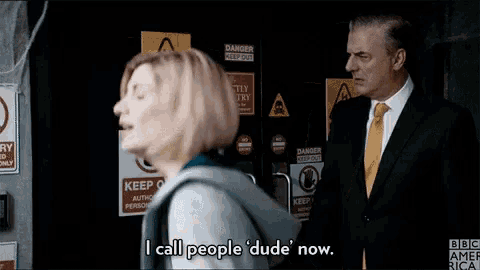 a man in a suit and tie is standing next to a woman who is saying i call people dude now