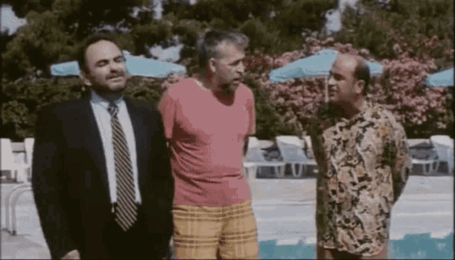 three men are standing next to each other next to a pool .