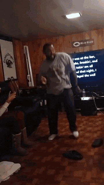 a man is dancing in a living room with a man cave sign on the wall behind him