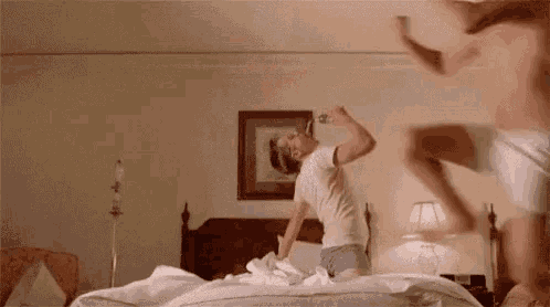 a man and a woman are having a pillow fight on a bed .
