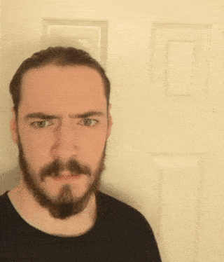 a man with a beard and mustache is standing in front of a door and making a funny face .