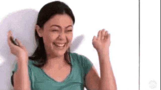 a woman in a green shirt is laughing and holding a cell phone .