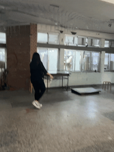 a woman is jumping in an empty room with a table and chairs in the background