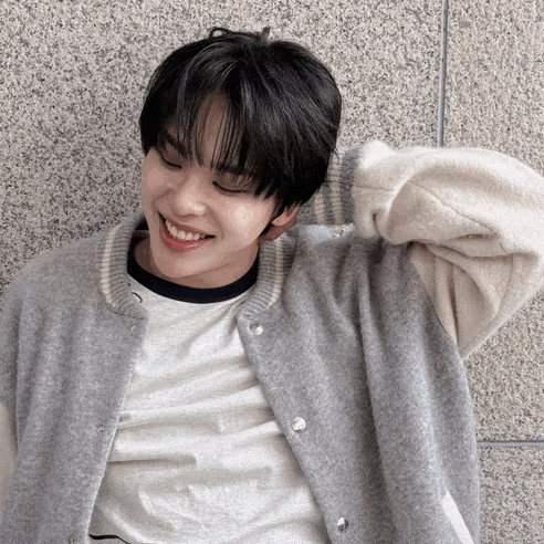 a young man wearing a gray jacket and a white shirt smiles