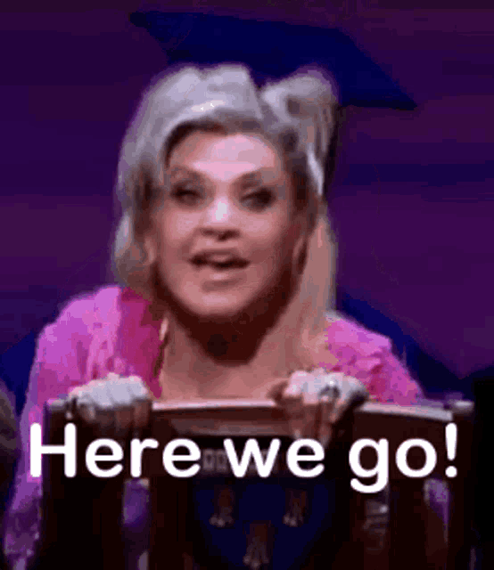 a woman in a graduation cap is holding a podium and says `` here we go '' .