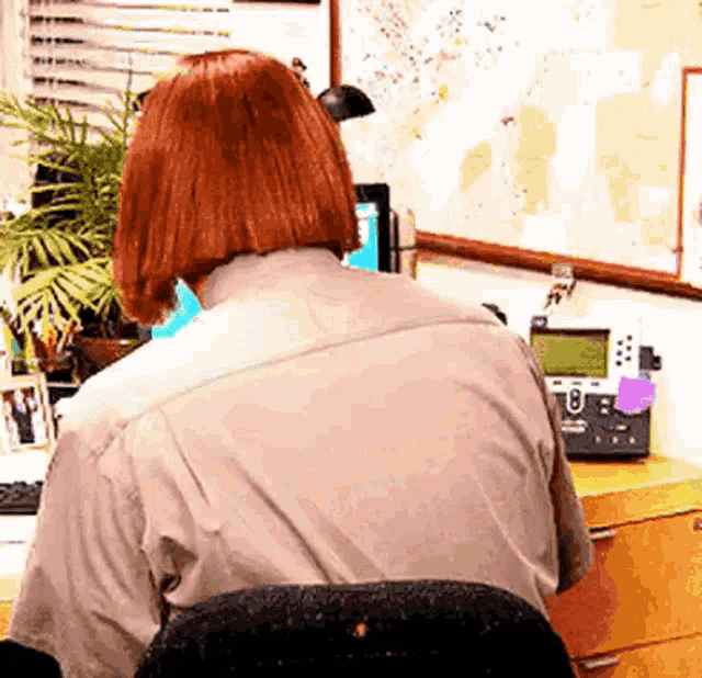 a woman with red hair is sitting at a desk in front of a computer and a telephone .