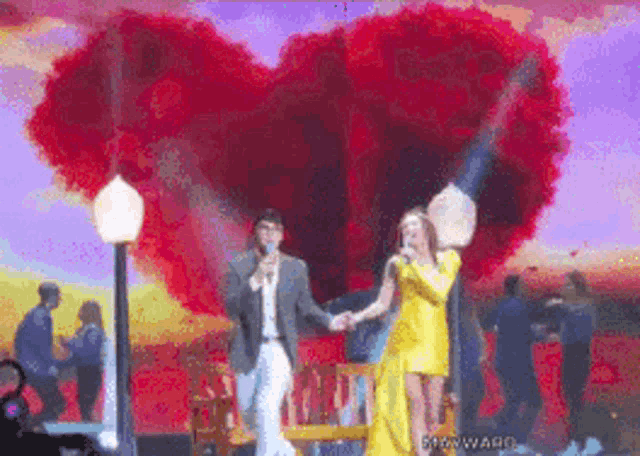 a man and a woman holding hands in front of a large heart