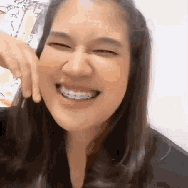 a woman with braces is smiling with her eyes closed and her hand on her face .