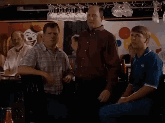 a group of men are standing in a bar with a clown in the background .