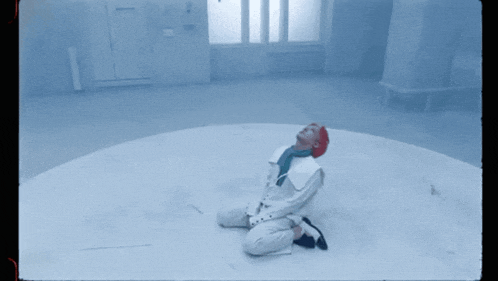 a man in a white suit and red hat is kneeling down in a room
