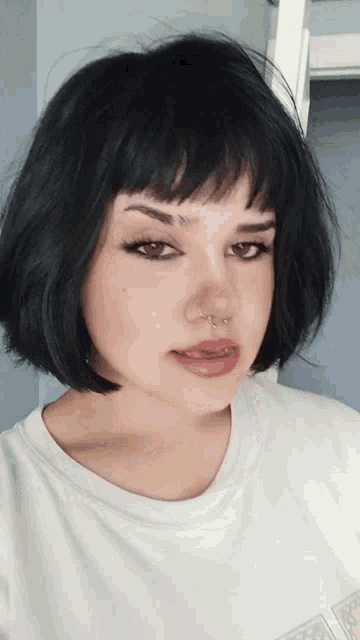 a woman with short black hair and a nose ring is wearing a white shirt