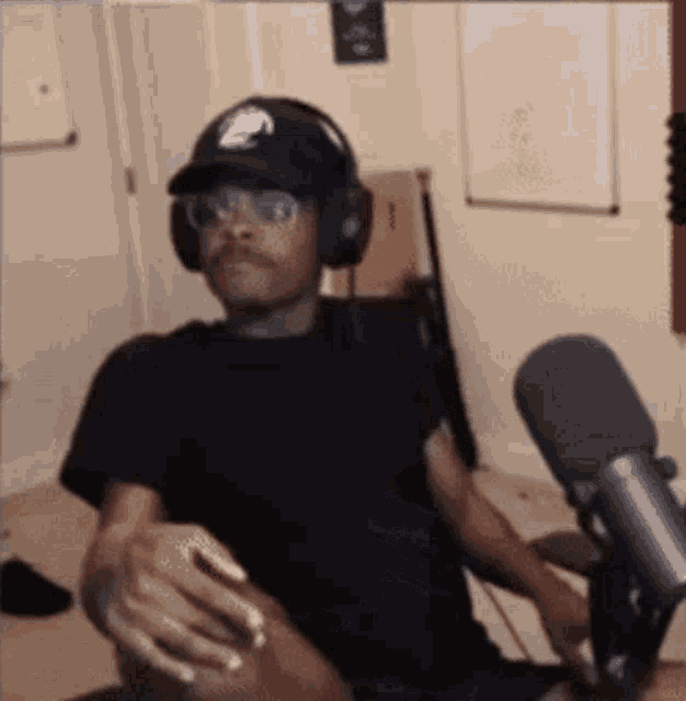 a man wearing headphones and a hat is sitting in front of a microphone in a room .
