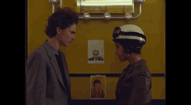 a man and a woman are looking at each other with a picture of a man on the wall behind them