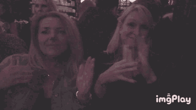 two women applauding in a dark room with imgplay in the lower right corner