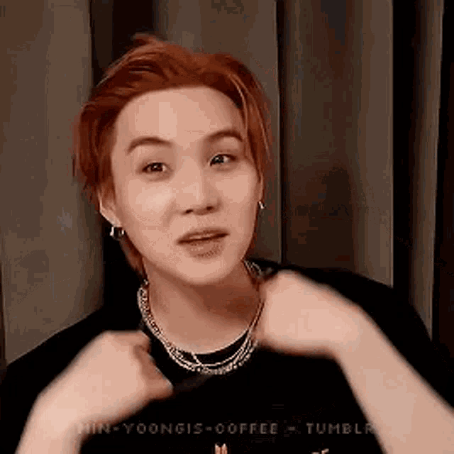 a young man with red hair is wearing a necklace and earrings and making a funny face .