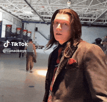 a man with long hair is wearing a suit and tie and has a tiktok icon above his head