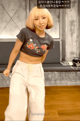 a woman wearing a crop top and white pants is dancing in a room