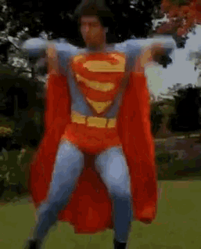 a man in a superman costume is dancing in a park