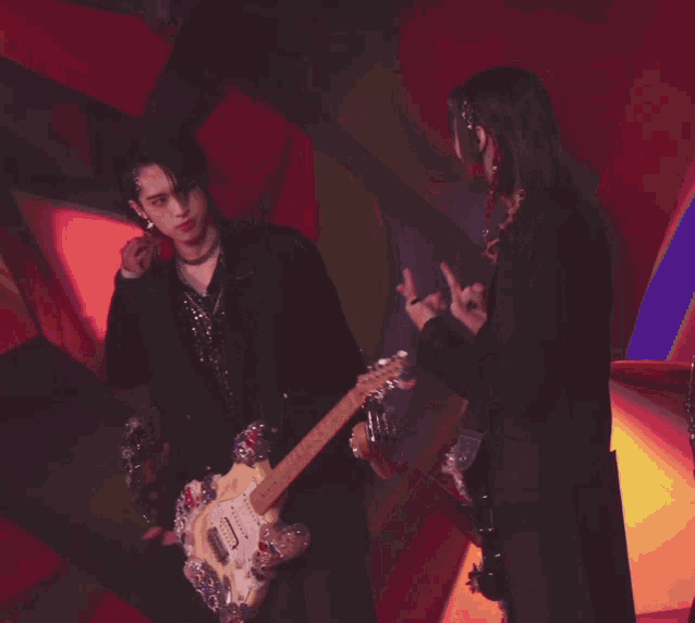two men are playing guitars in front of a colorful wall