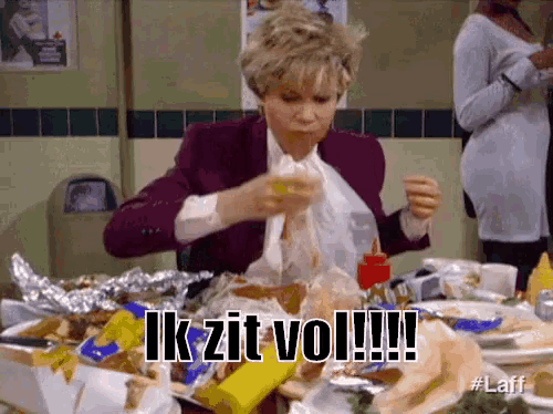 a woman is sitting at a table with a bunch of food and a sign that says ik zit vol .