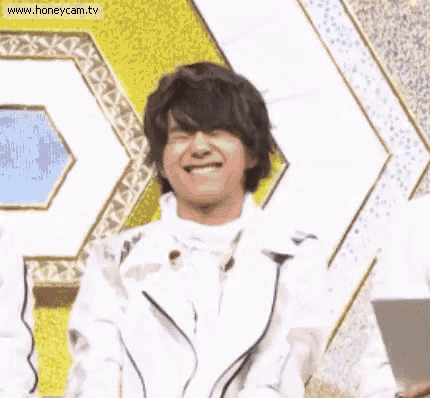 a man in a white jacket is smiling with his eyes closed in front of a yellow and white background .