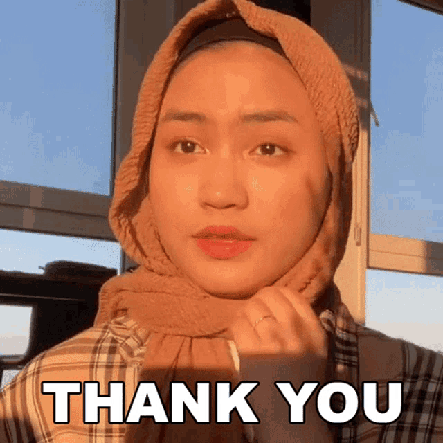 a woman wearing a hijab says " thank you " in front of a window