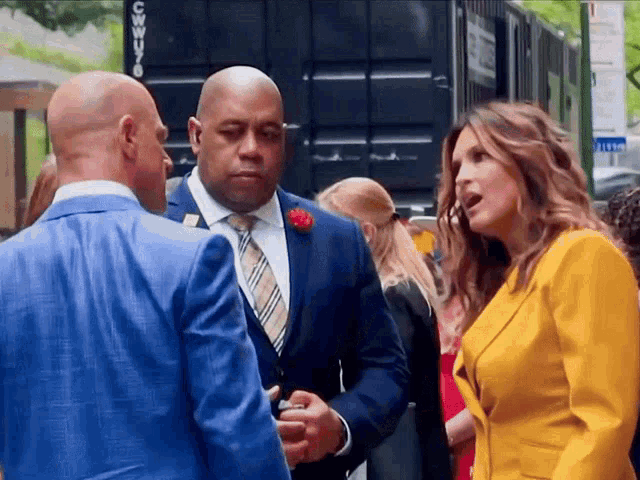 a man in a blue suit and tie is talking to a woman in a yellow jacket