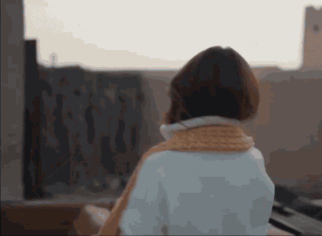 a woman wearing a white coat and a yellow scarf is looking out a window