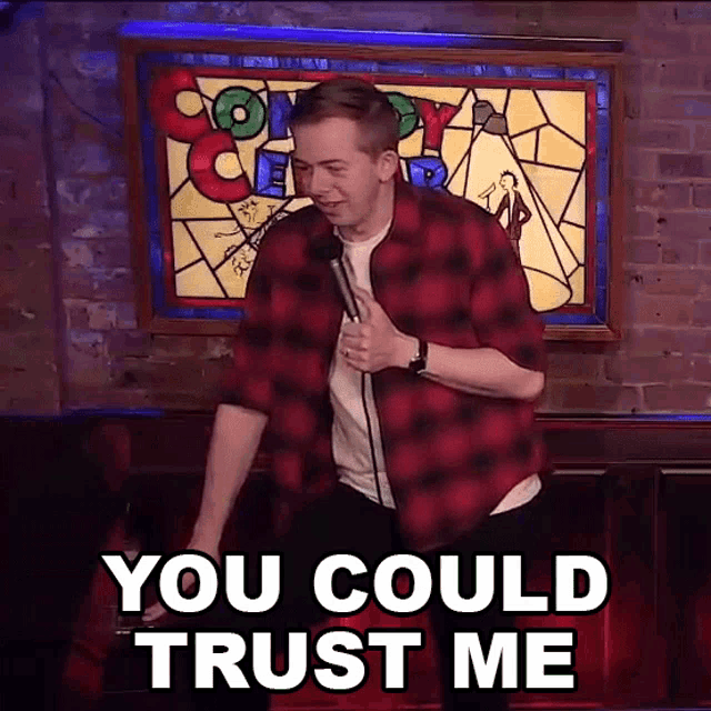 a man in a red plaid shirt is holding a microphone and says you could trust me