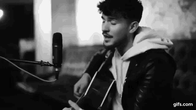 a young man is singing into a microphone while playing an acoustic guitar .
