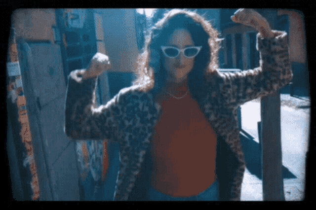 a woman wearing sunglasses and a leopard print coat is flexing her muscles