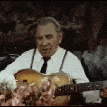 a man in a white shirt and tie is playing a guitar in a dark room .