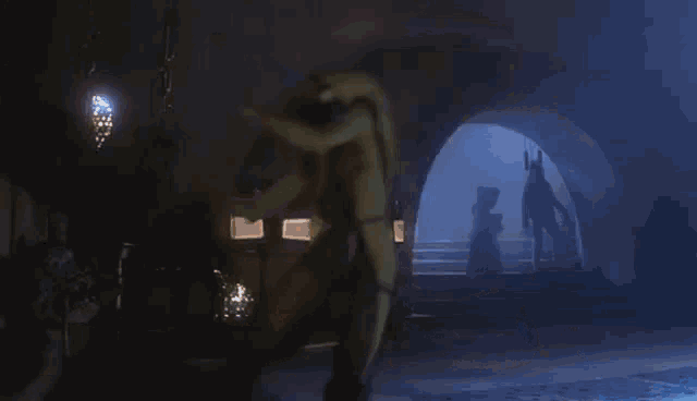 a group of people are standing in a dark room in a cave with a statue in the background .