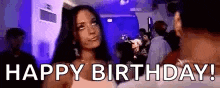 a woman is standing in a crowded room with the words `` happy birthday '' written on her face .