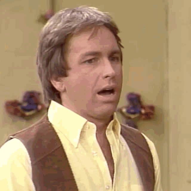 a man wearing a yellow shirt and brown vest is making a funny face .
