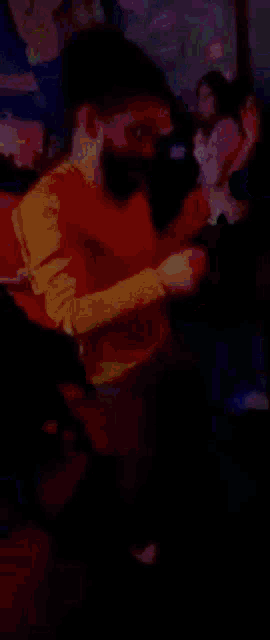 a man in a yellow shirt is dancing in a dark room with other people