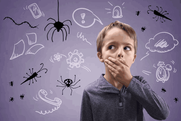 a young boy covering his mouth with his hand in front of drawings of spiders and other things