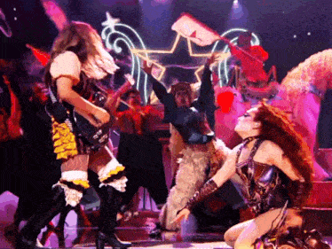 a group of people are dancing on a stage and one of them has a guitar in her hand