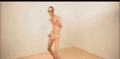 a shirtless man wearing sunglasses is sitting on an orange chair holding a glass of wine .