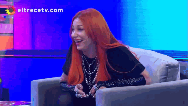 a woman with red hair is sitting in a chair with the website eltrecetv.com behind her