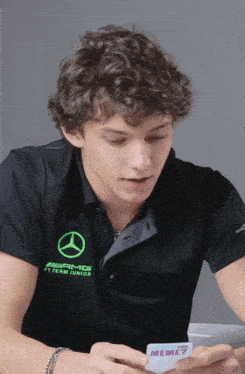a young man wearing a mercedes f1 team junior shirt is looking at his phone