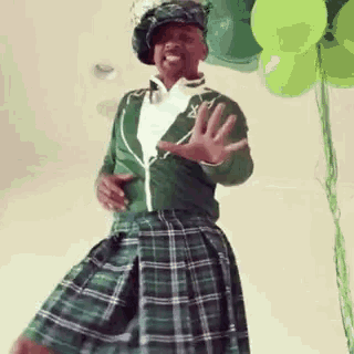 a man in a kilt is standing in front of balloons .