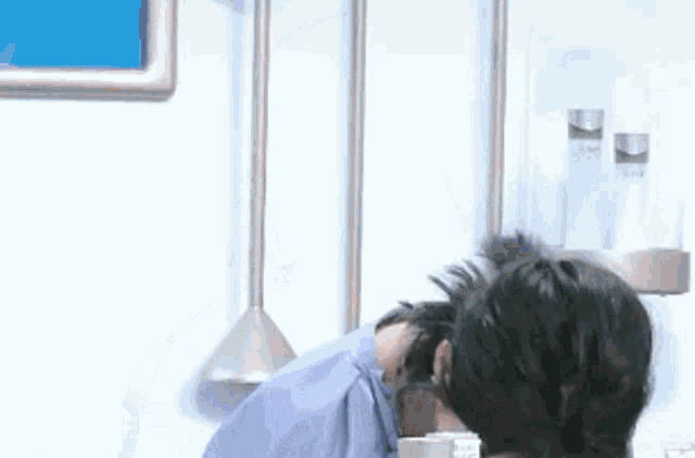 a man in a blue shirt is sitting in a kitchen with his head down .